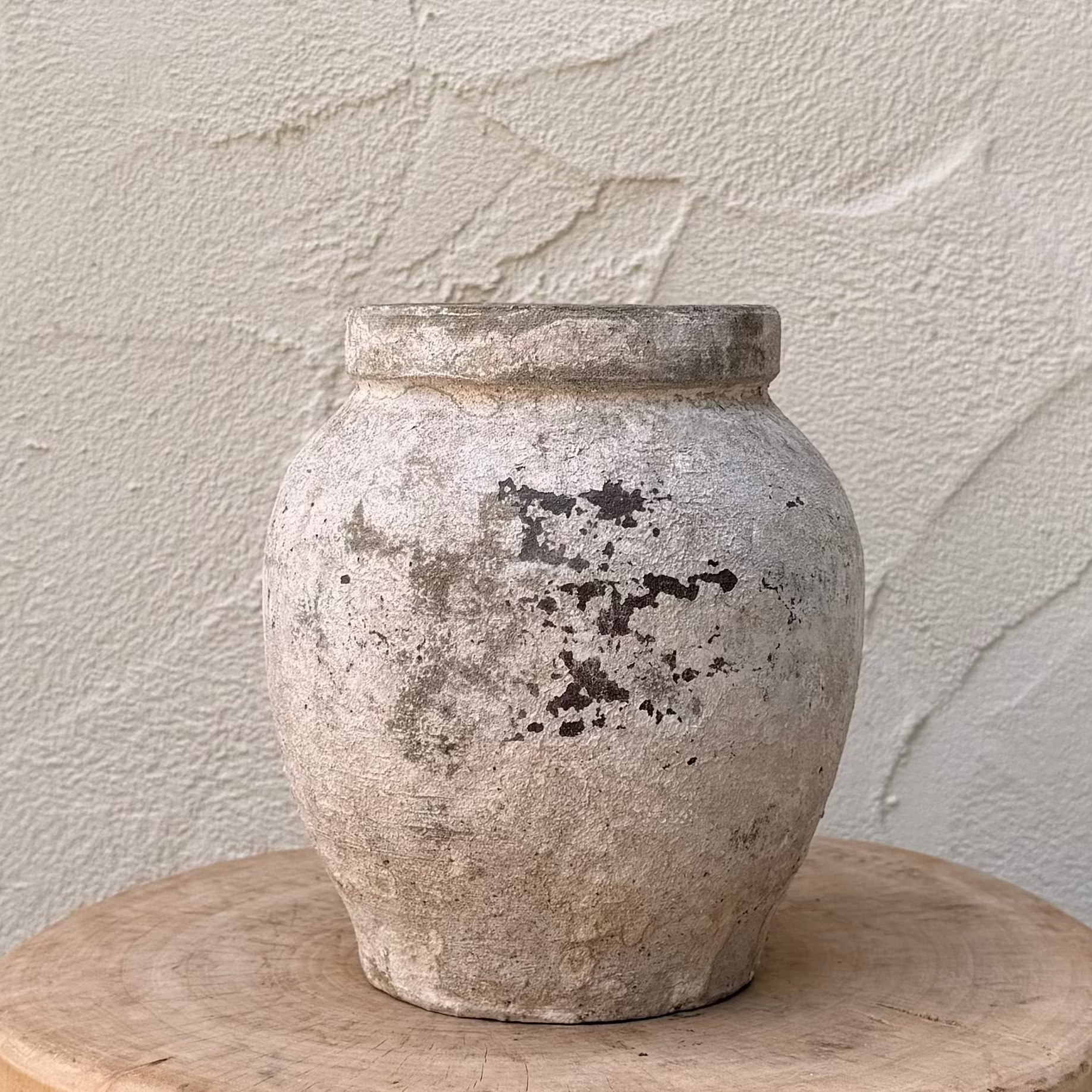 Terracotta pot on a wooden stool against a textured wall.