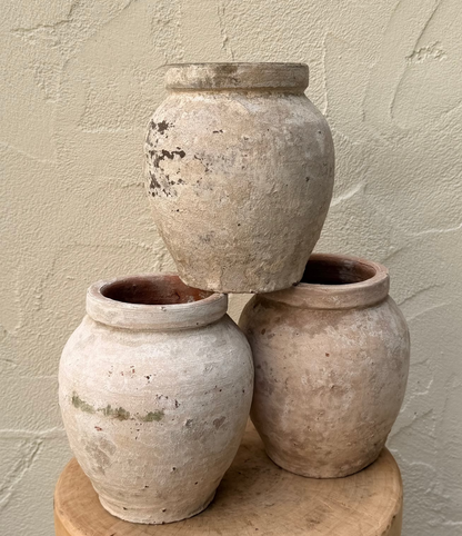 Three stacked ceramic pots on a wooden stool against a textured wall.