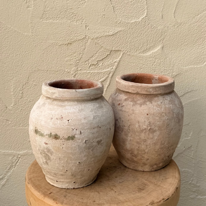Two terracotta pots on a wooden stool against a textured beige wall.