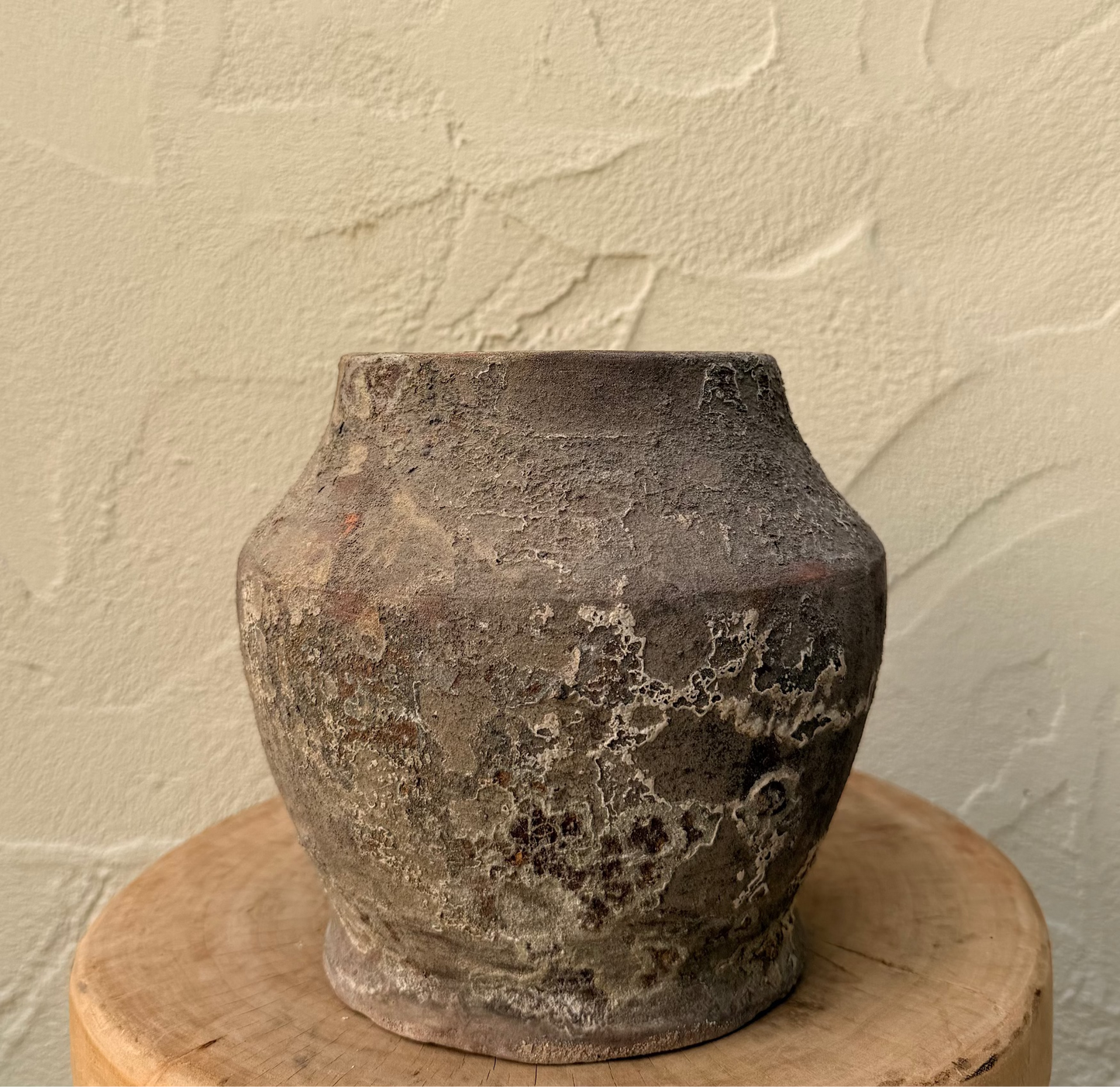 Vintage terracotta pot on a wooden stand against a textured beige wall