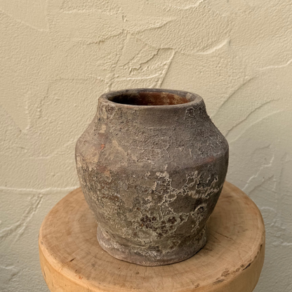 Vintage terracotta pot on a wooden stand against a textured beige wall