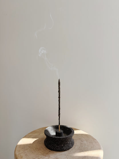 Incense stick burning in a black holder on a light wooden surface with a plain background